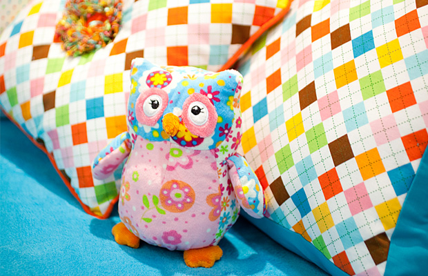 Colorful plush owl toy on patterned pillows, bright multicolor tones, playful cheerful mood
